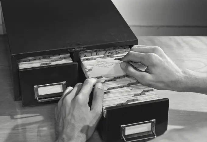 Vintage photograph. High angle view of a businessman filing cards in drawer