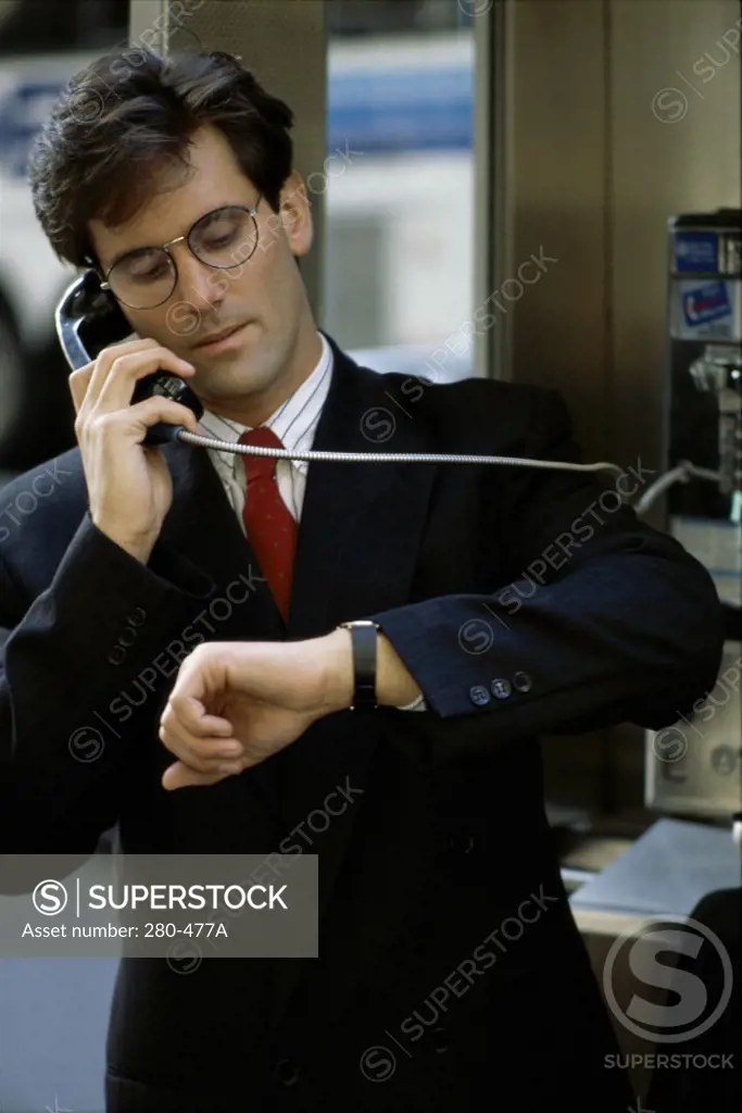 Businessman checking the time on his wristwatch and talking on the payphone
