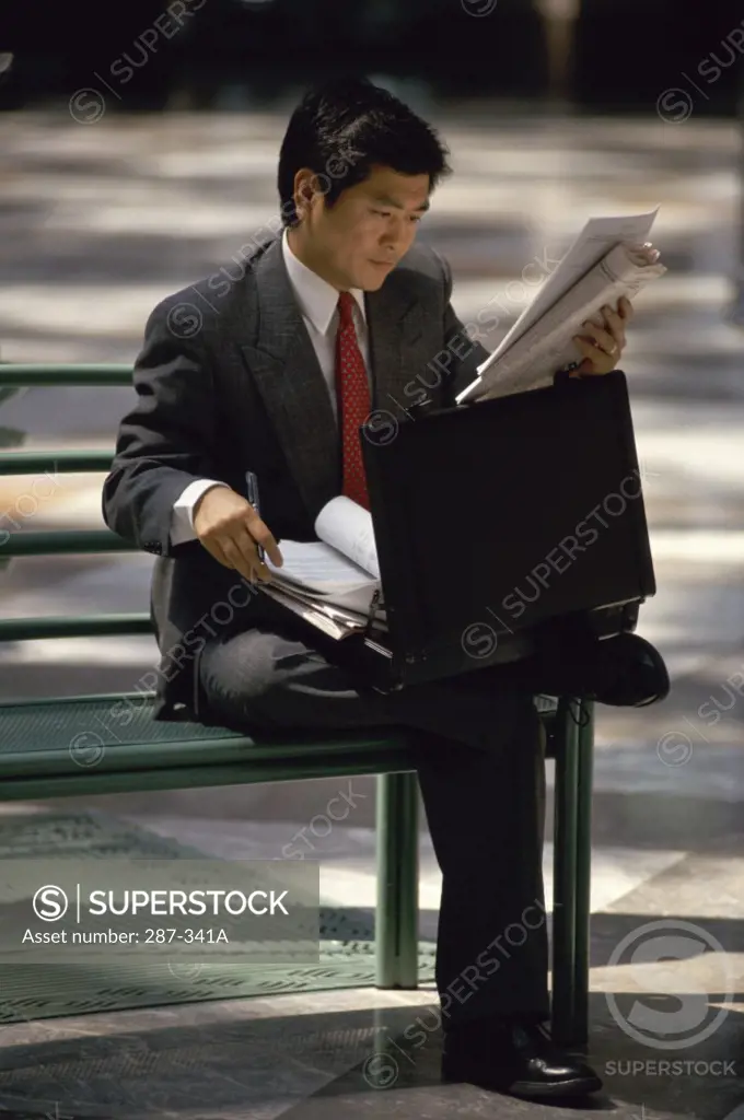 Businessman sitting on a bench and reading a newspaper