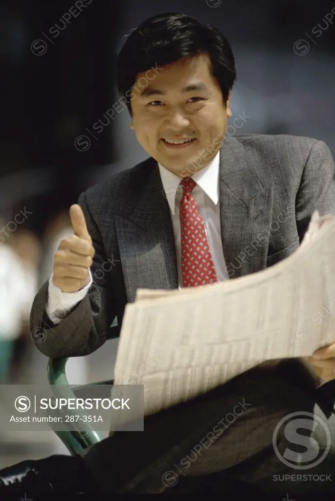 Businessman holding a newspaper and making a thumbs up sign