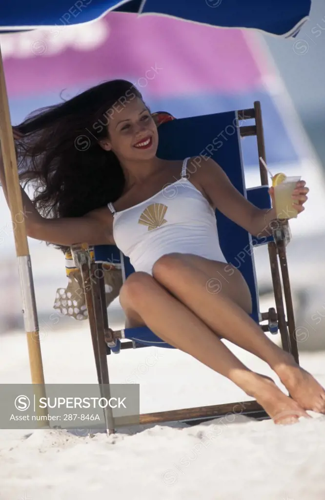 Young woman sitting on a chaise longue under a beach umbrella