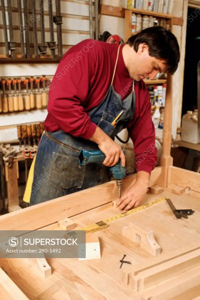 Carpenter using an electric drill on a plank