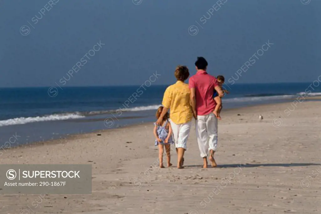 Rear view of a man and woman with their son and daughter strolling on the beach