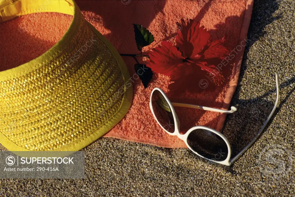 Close-up of a visor with a hibiscus and sunglasses on a beach towel
