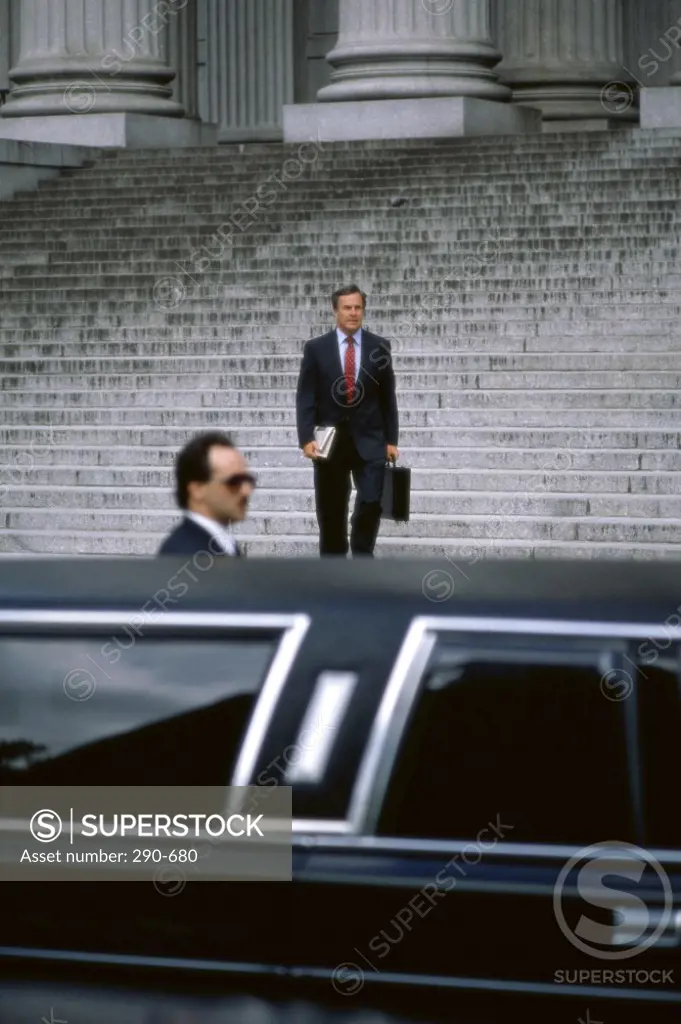 Businessman moving down steps and his driver standing beside a car