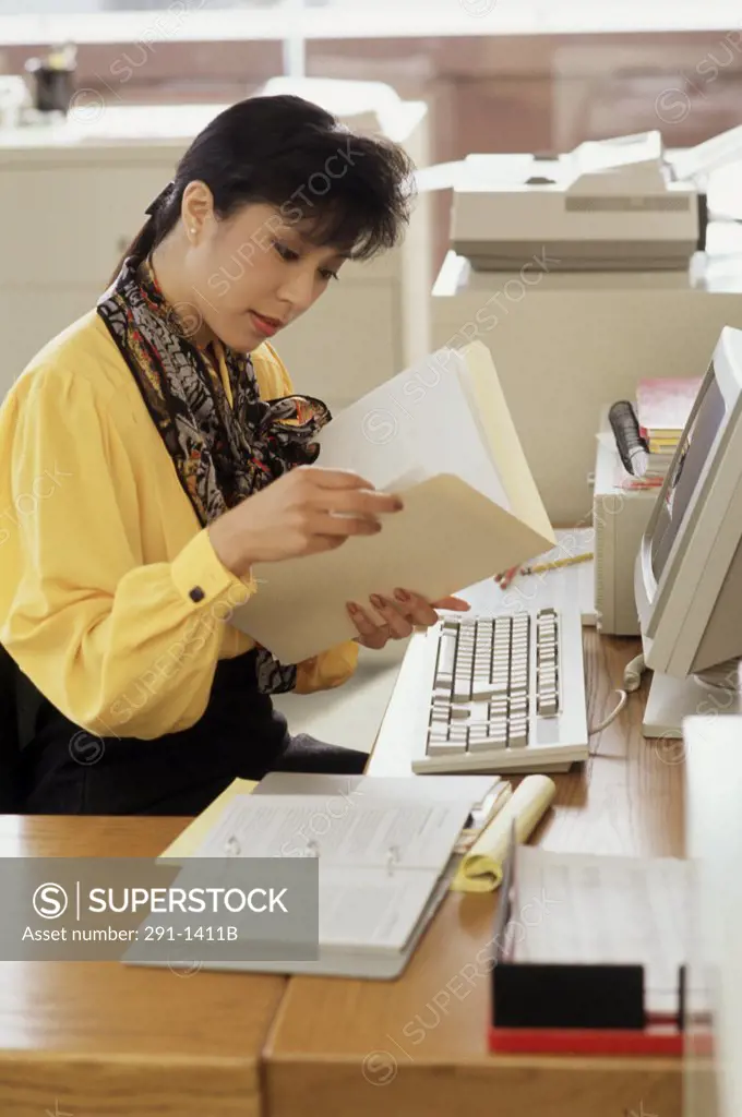 Side profile of a businesswoman sitting in front of a computer and reading a file