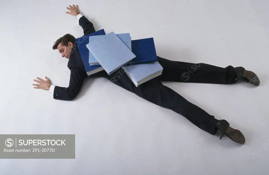 High angle view of a businessman lying down with files on his back
