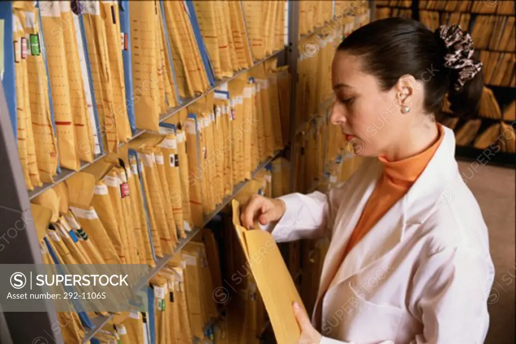 Side profile of a female nurse holding a medical record in front of a shelf