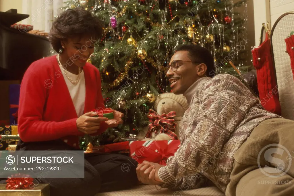 Mid adult woman opening a Christmas present with a mid adult man lying beside her