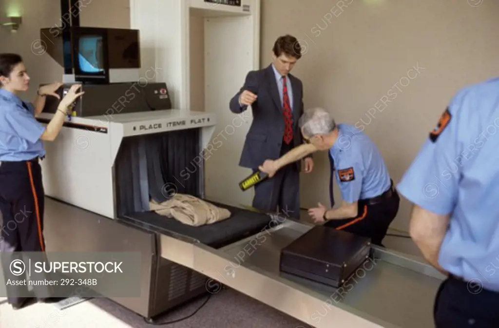 Security guard checking a young man with a metal detector in an airport