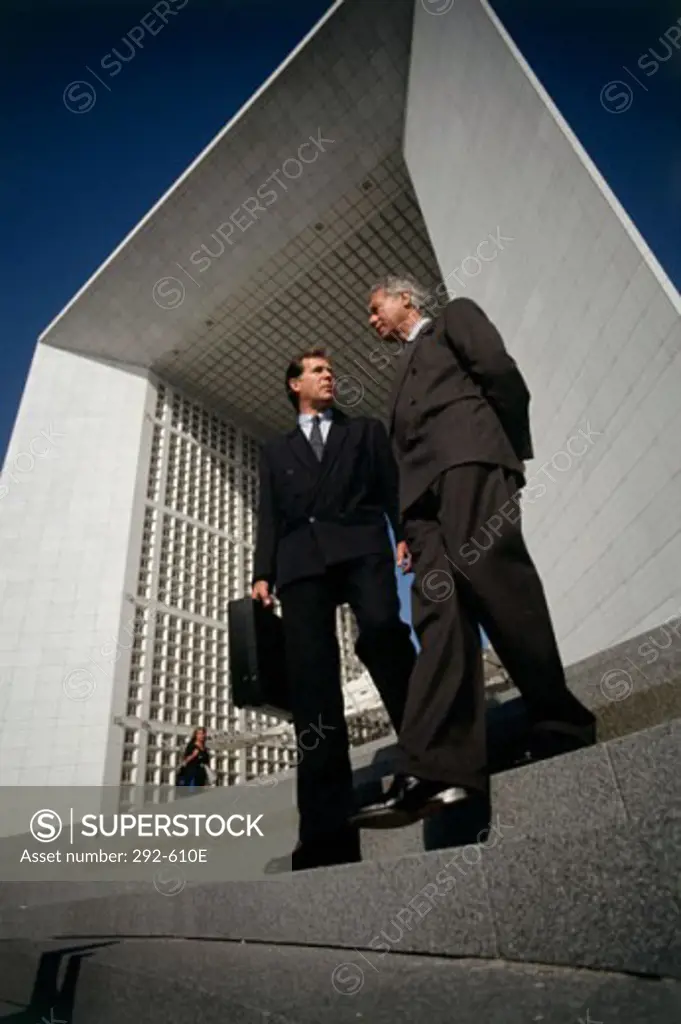 Low angle view of two businessmen moving down steps and talking to each other, La Defense, Paris, France