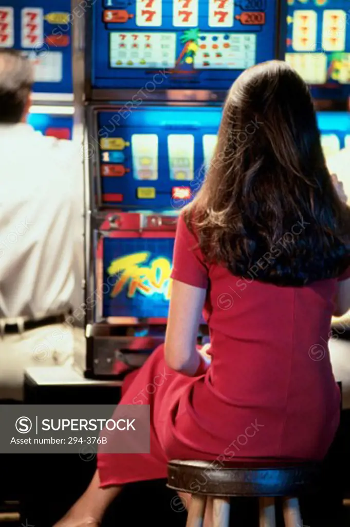 Rear view of a woman playing a slot machine in a casino