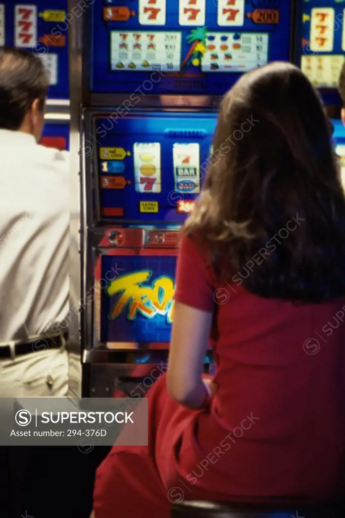 Rear view of a woman and a man playing slot machines in a casino
