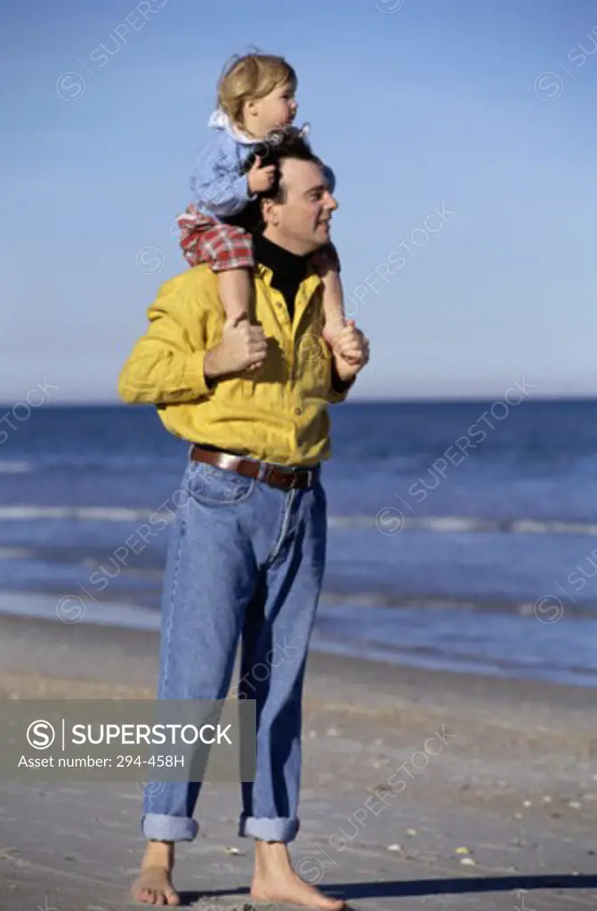 Mid adult man carrying his daughter on his shoulders and standing on the beach