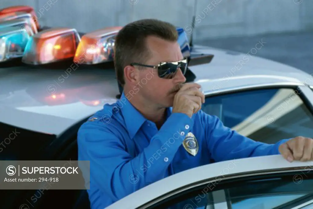Police officer standing near a car and speaking into a radio handset