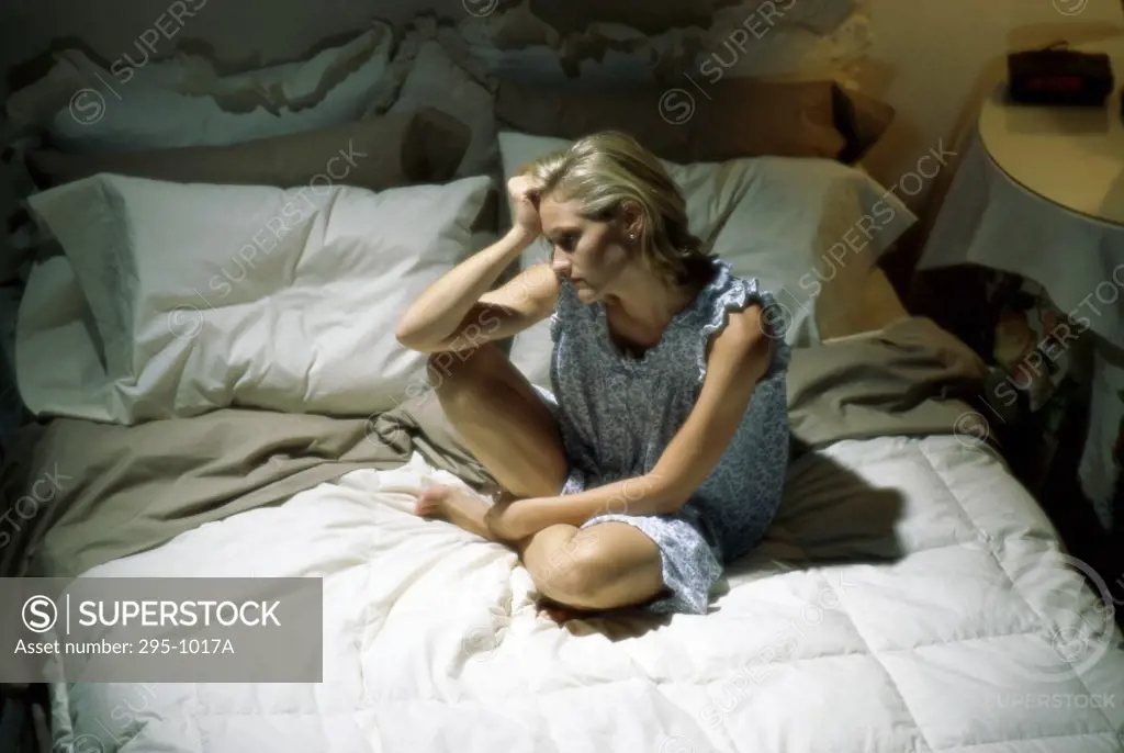 High angle view of a young woman sitting on the bed and looking upset