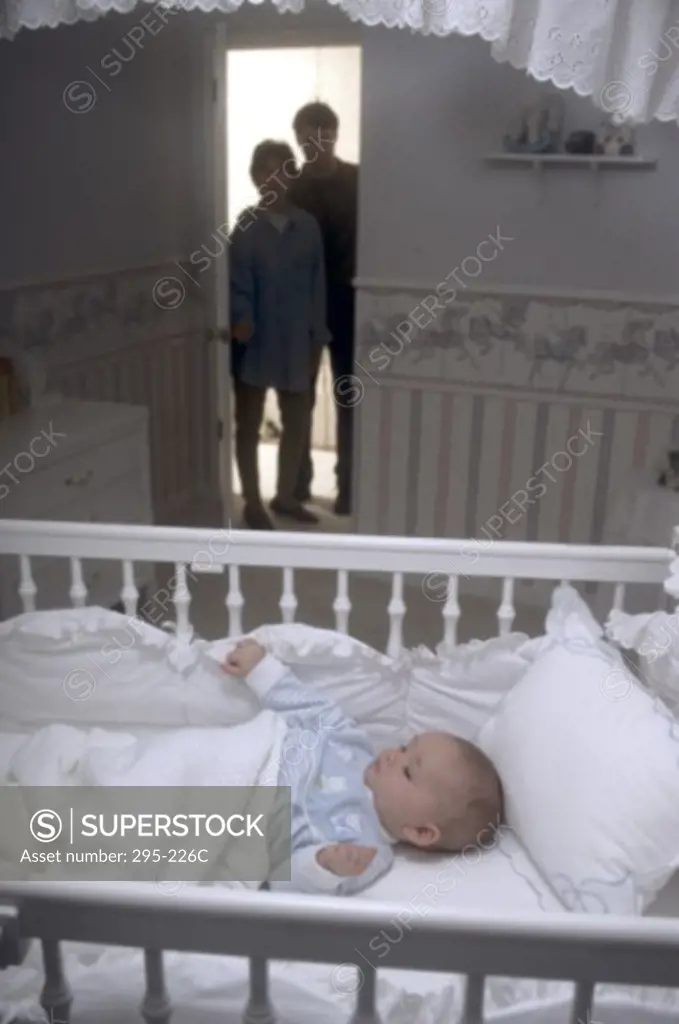 Silhouette of a young couple peeking at their son sleeping in a crib