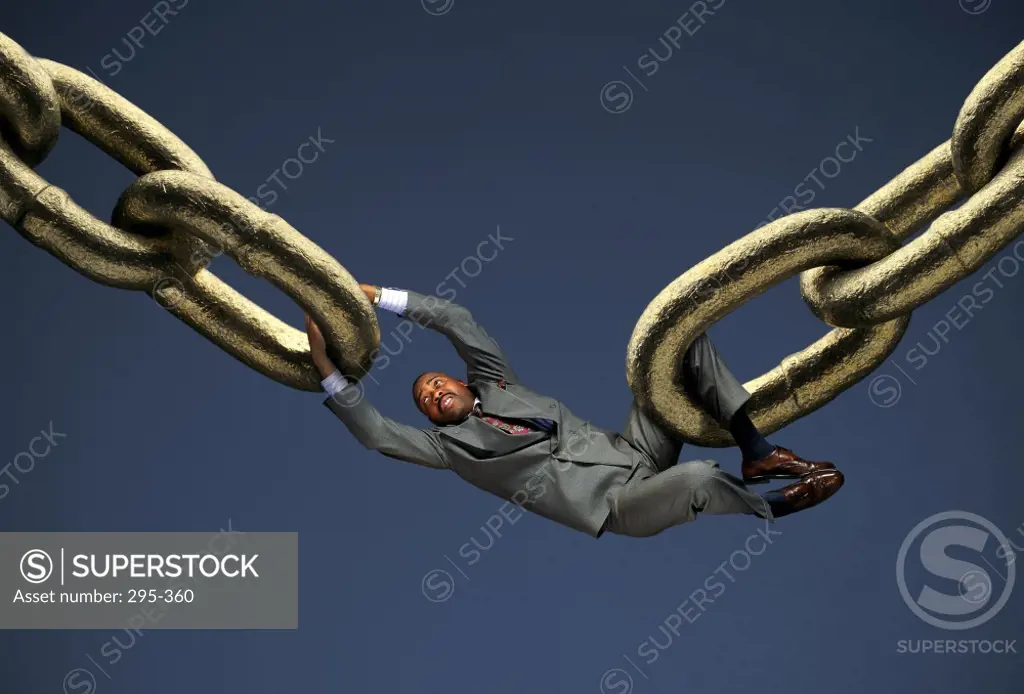 Businessman hanging between two chains