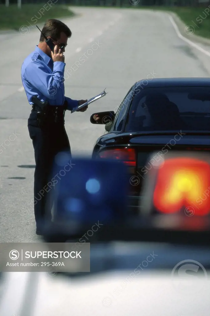 Police officer standing near a car talking on a walkie-talkie