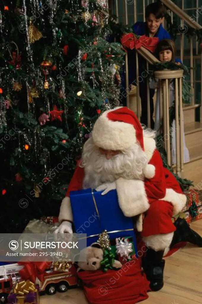 Santa Claus putting Christmas presents under a Christmas tree