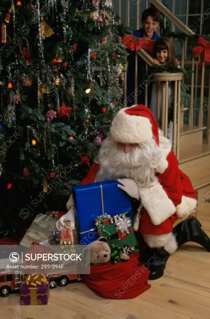 Santa Claus putting Christmas presents under a Christmas tree