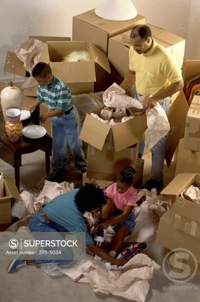 Mid adult couple with their children unpacking cardboard boxes in their new house
