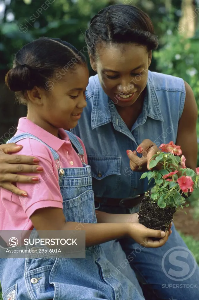 Girl holding a plant with her mother standing beside her