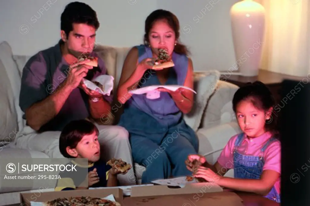Mid adult couple and their children eating pizza and watching television