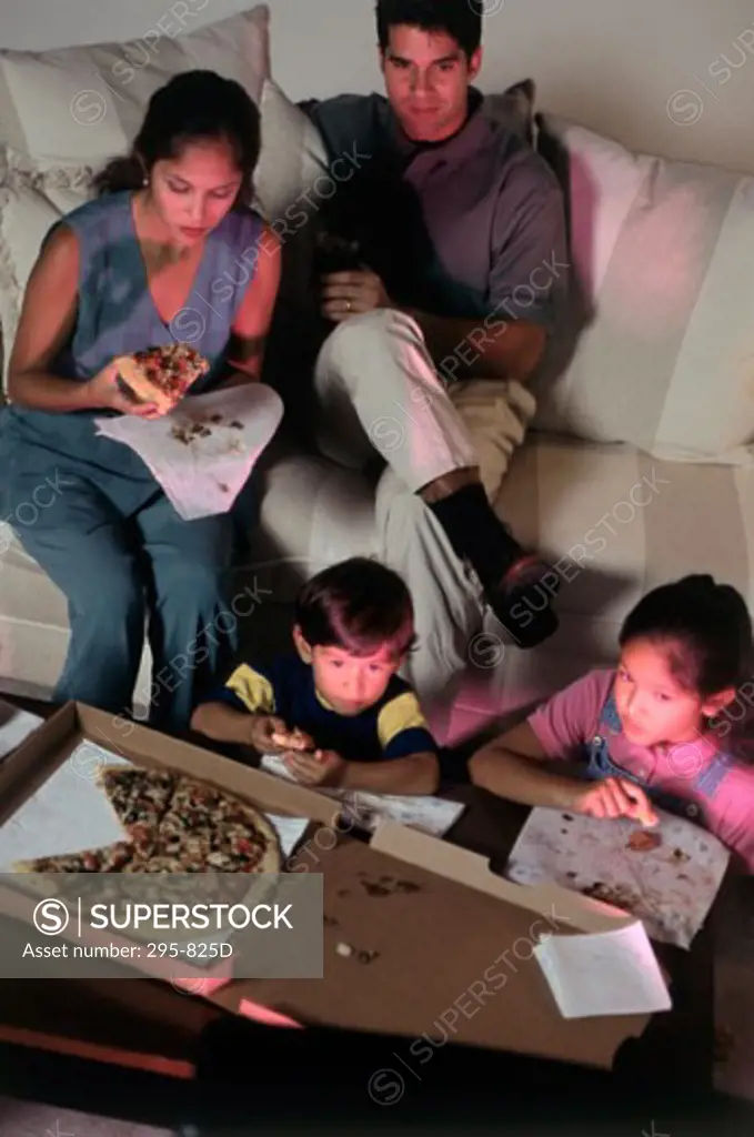 High angle view of a mid adult couple and their children eating pizza and watching television