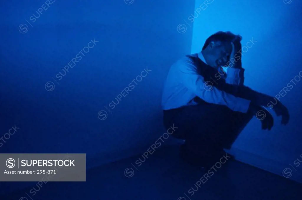 Businessman crouching in the corner of a room and crying
