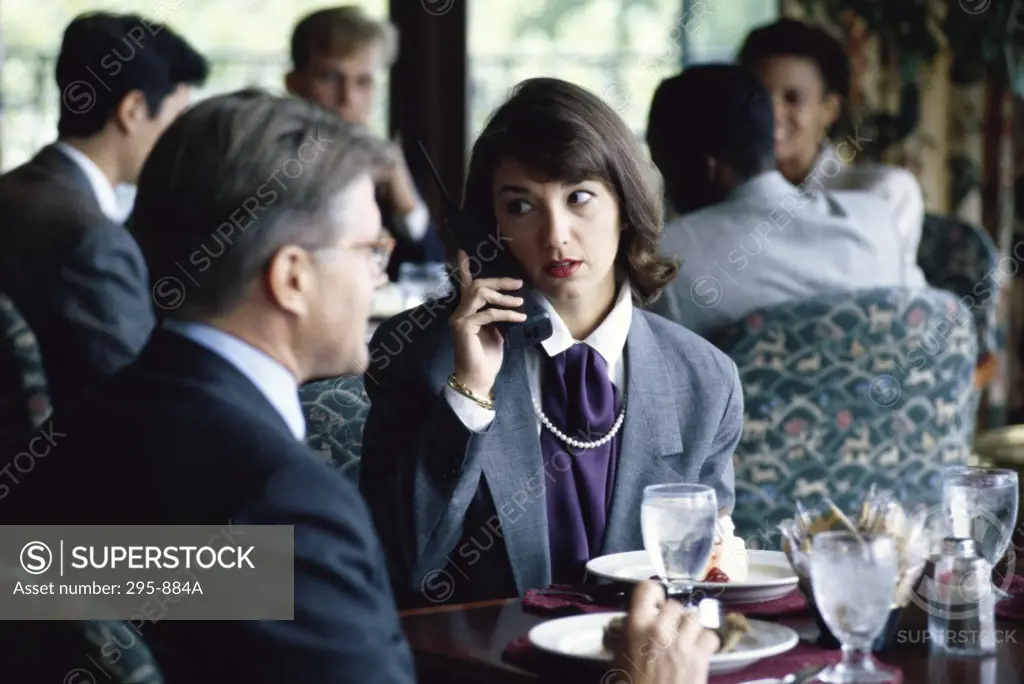 Businesswoman using a cordless phone and a businessman sitting beside her in a restaurant