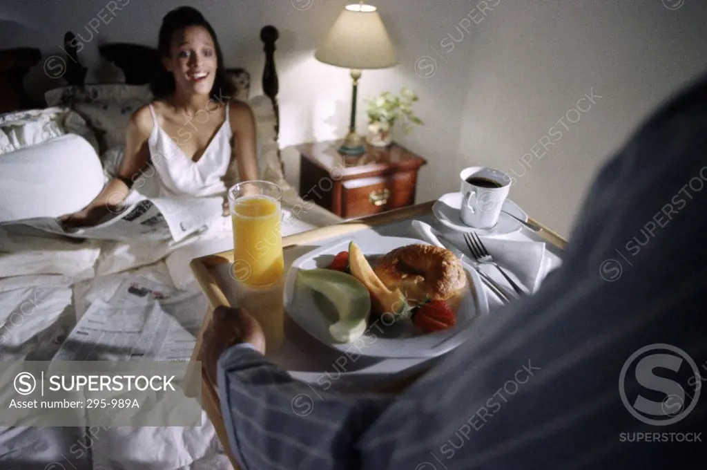 Young woman sitting on the bed and surprisingly looking at breakfast