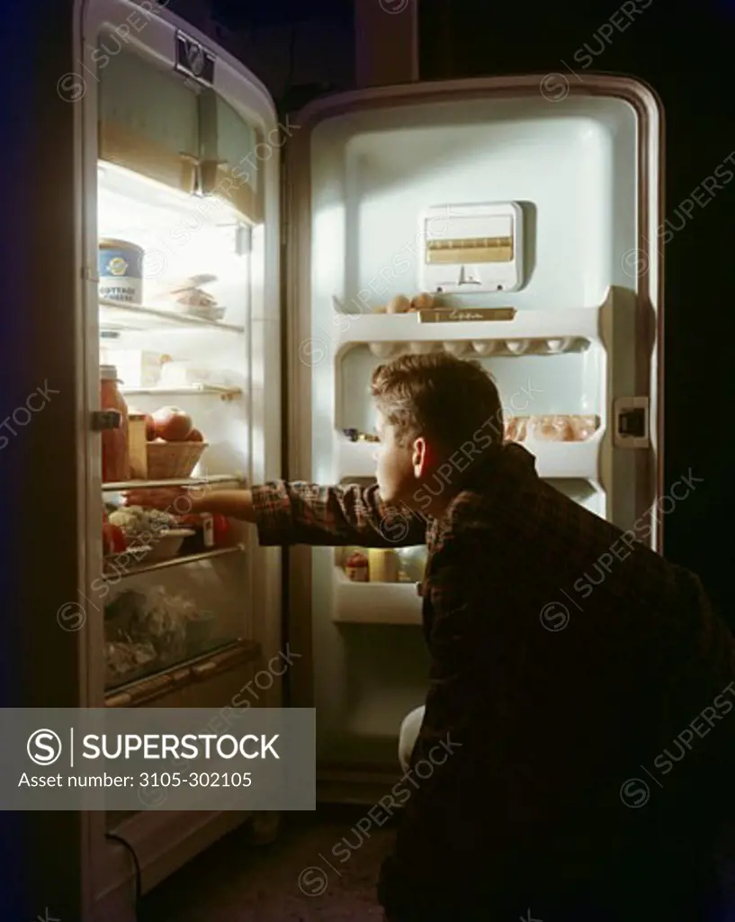 Side profile of a boy taking food from a refrigerator