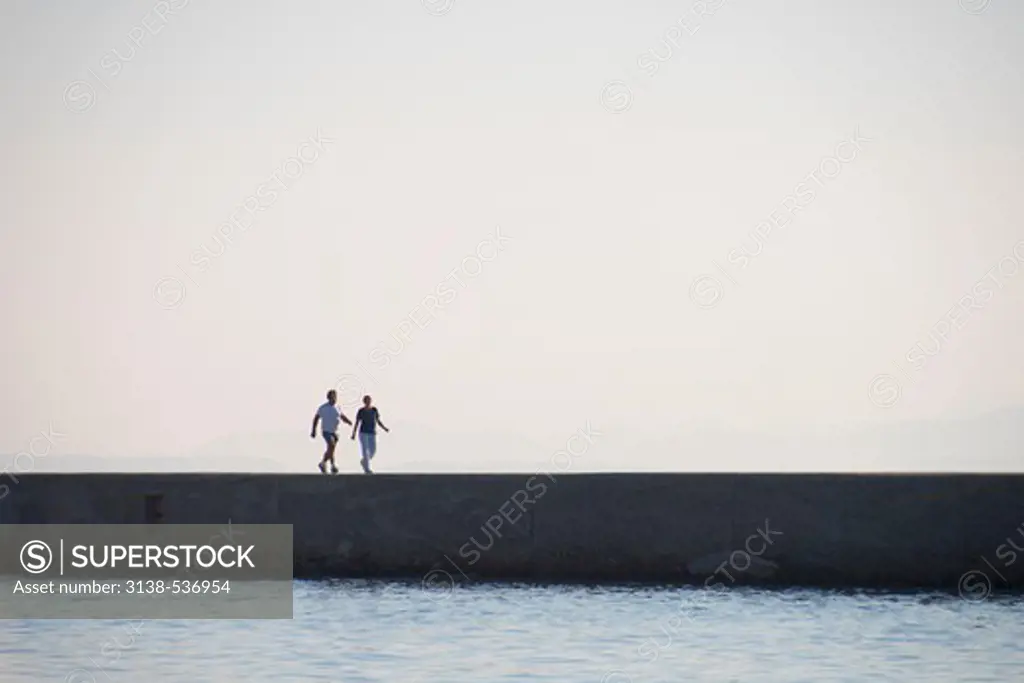 Two people walking on a jetty at dawn, Mytilene, Lesbos, Greece