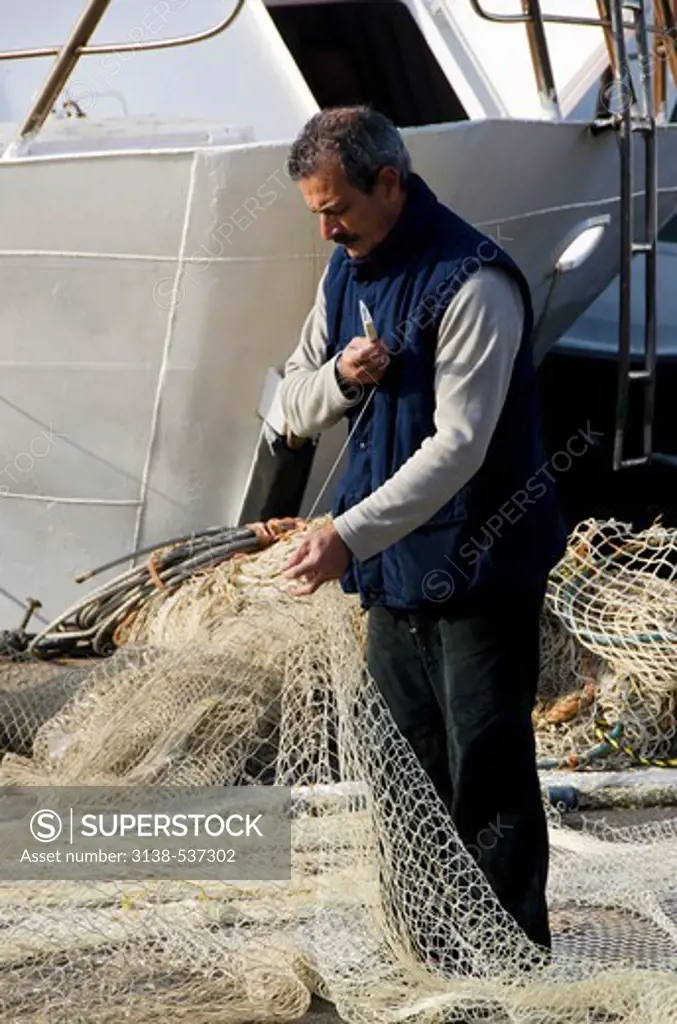 Fisherman repairing fishing net at a harbor, Livorno, Tuscany, Italy