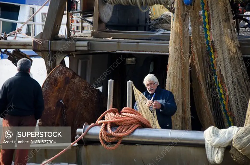 Fisherman repairs fish net in small boat harbor, Livorno, Italy