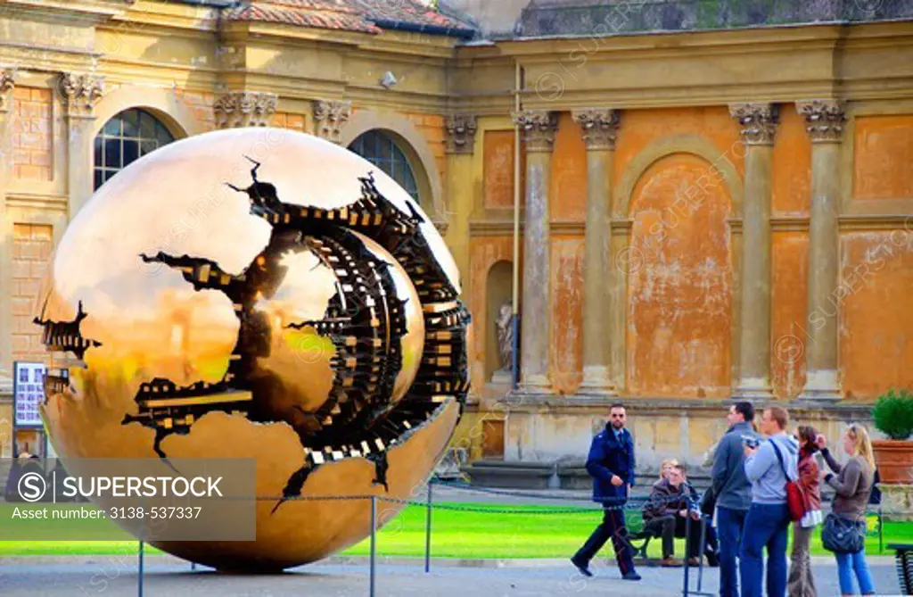 Tourists contemplate huge bronze spinning globe sculpture of Sphere Within Sphere, Vatican Museums, Vatican City