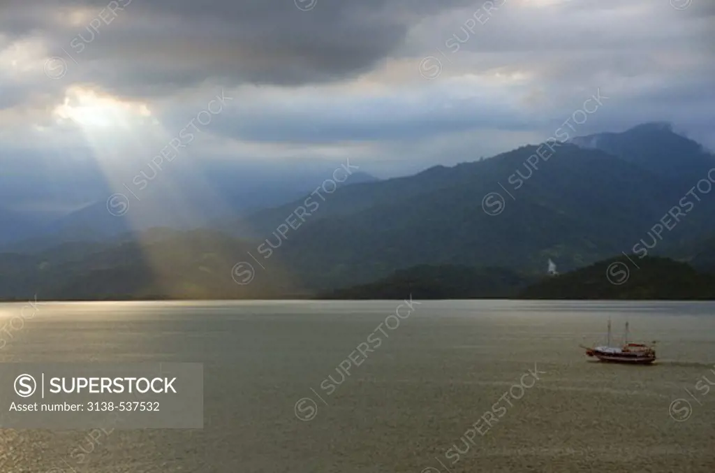 Mystical sunrays from the cloudy sky over the bay with a boat, Paraty, Rio De Janeiro, Brazil