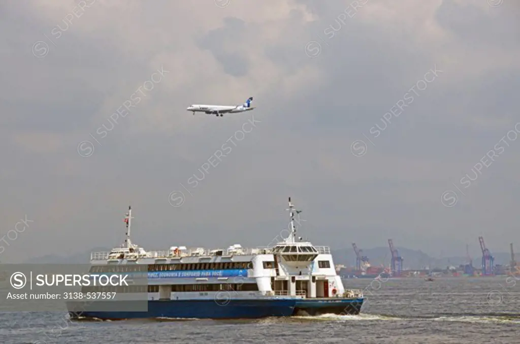Airplane in flight over a ferry in the ocean, Niteroi, Rio De Janeiro, Guanabara Bay, Brazil