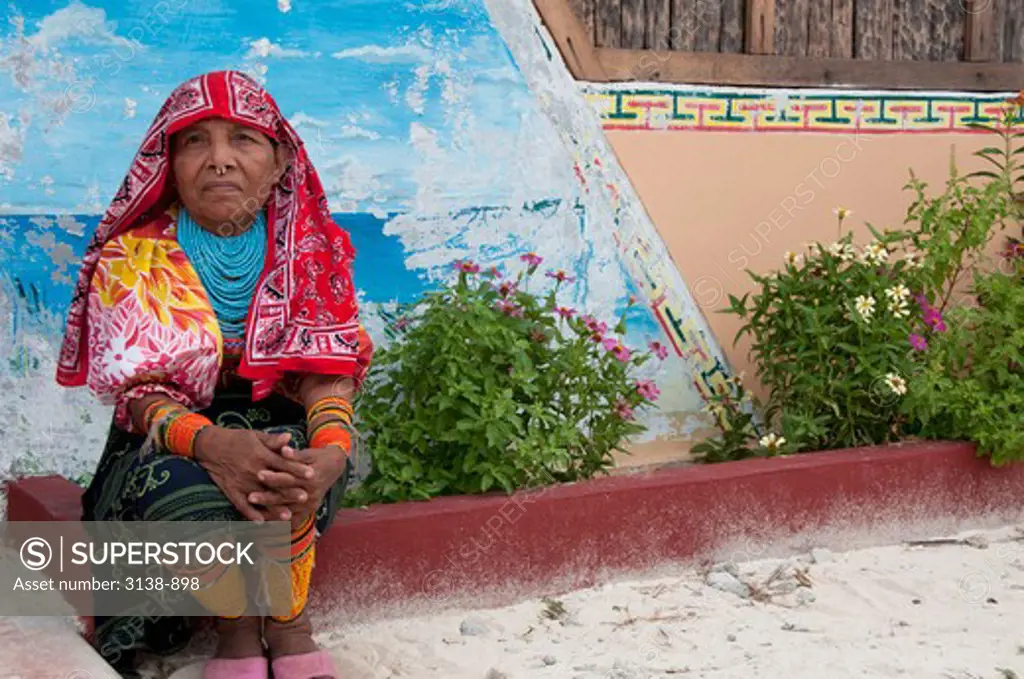 Woman in traditional dress sitting in front of a wall, San Blas Islands, Kuna Yala, Panama