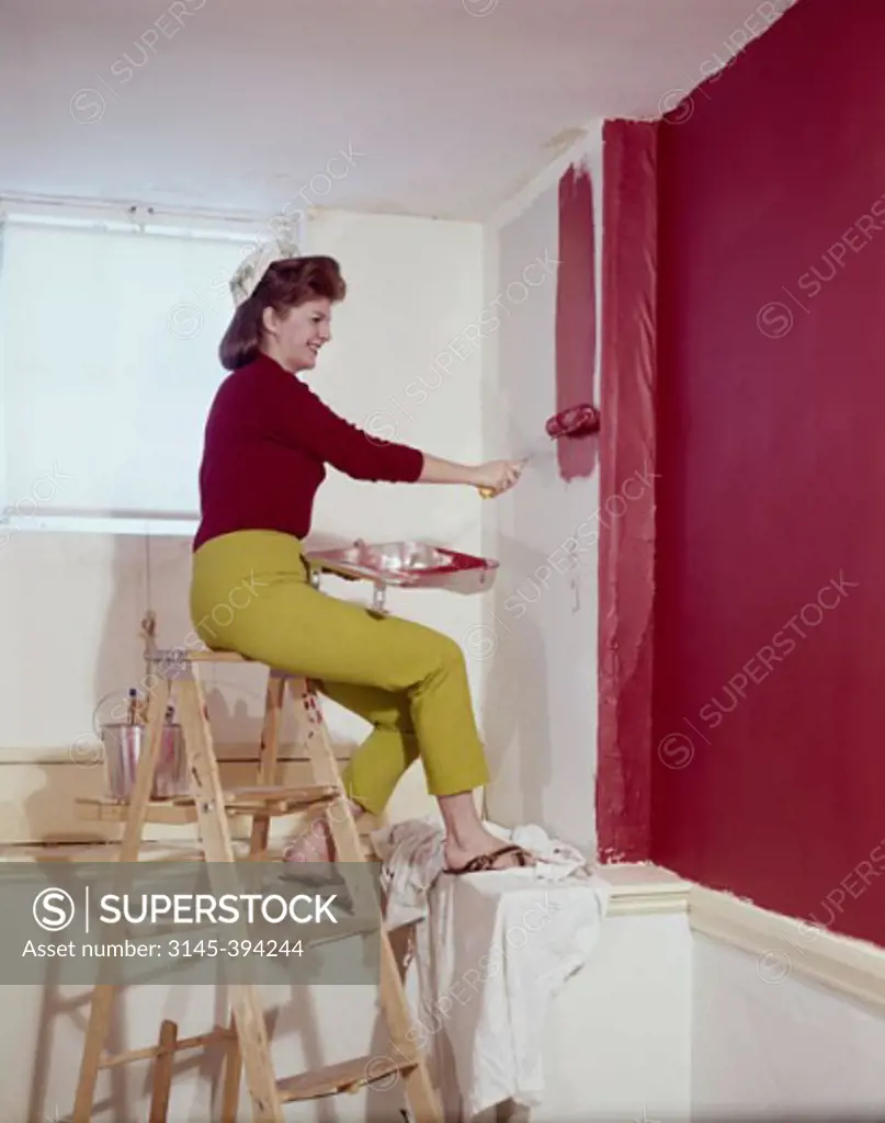 Side profile of a mid adult woman painting a wall with a paint roller