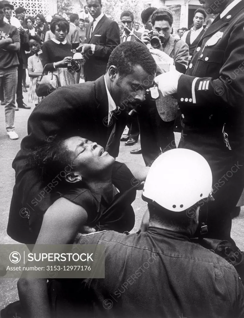 fainted woman helped by a friend and a police during the funeral march for martin luther king, at,lanta, 1968