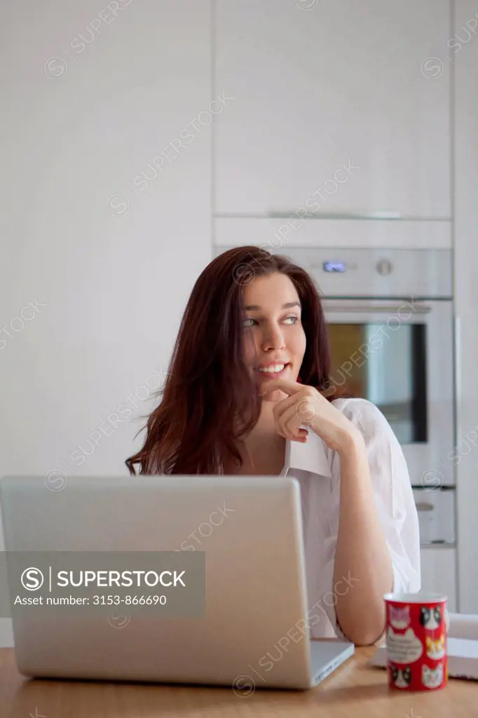 Woman in kitchen with laptop and cup of tea