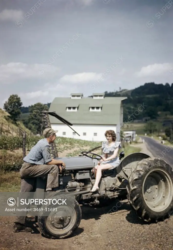 Young woman sitting on a tractor with a young man standing in front of her