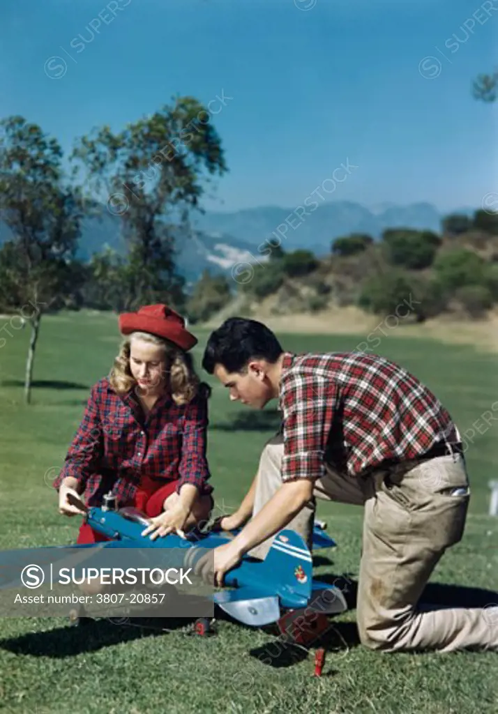 Teenage boy and a teenage girl repairing a model airplane in a park
