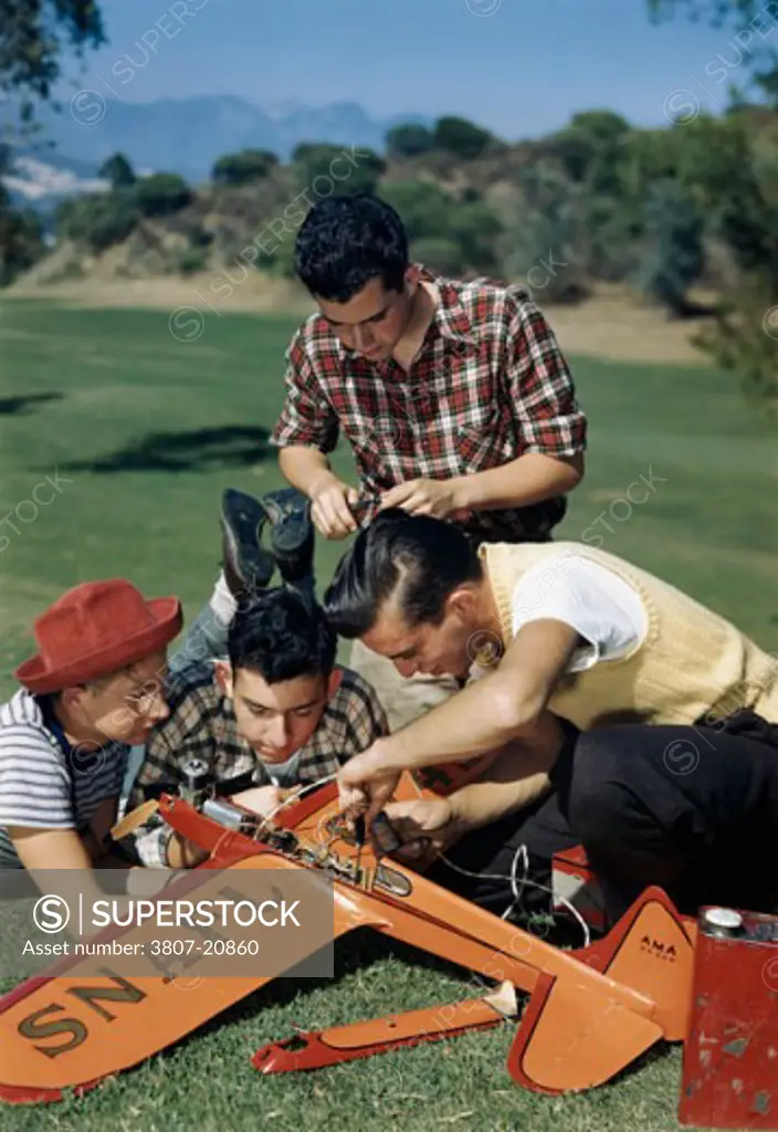 Four teenager boys repairing a model airplane in a park