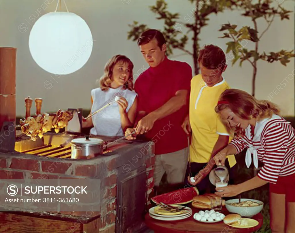 Two teenage couples preparing food on a barbecue grill