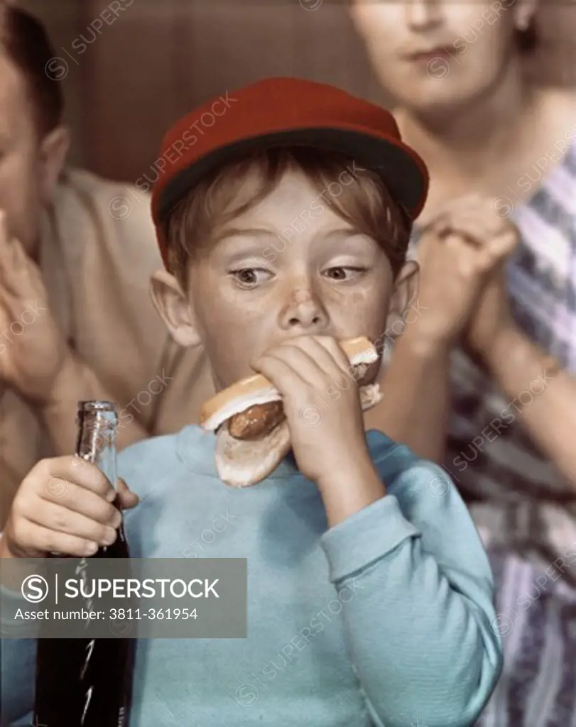 Close-up of a boy eating a hot dog and holding a bottle of soda