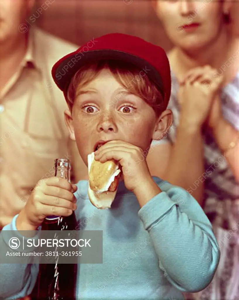 Close-up of a boy eating a hot dog and holding a bottle of soda