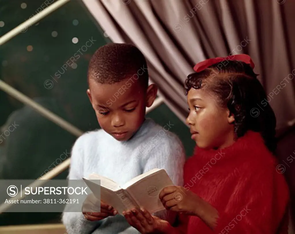 Close-up of a boy reading a book with his sister